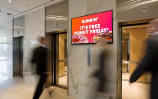 Digital out-of-home advertising screen displays promotional content in high-traffic elevator lobby location.