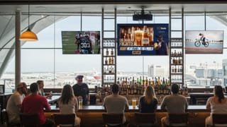 Airport bar patrons viewing Atmosphere TV screens displaying sports and Modelo beer ads programmatically