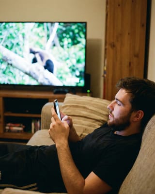 Viewer watches TV while scrolling phone, illustrating Netflix's distracted audience challenge