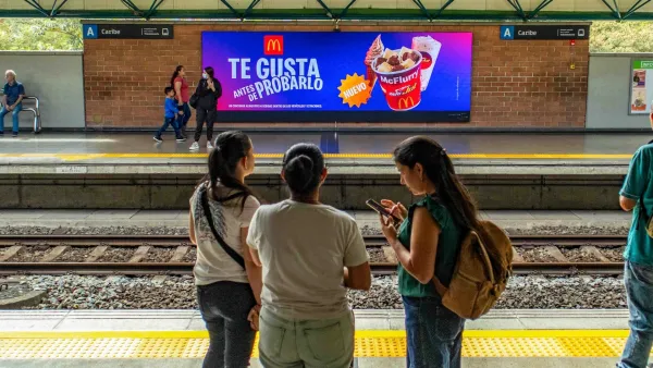 Digital screen displaying McDonald's ad at Colombian metro station with commuters on platform
